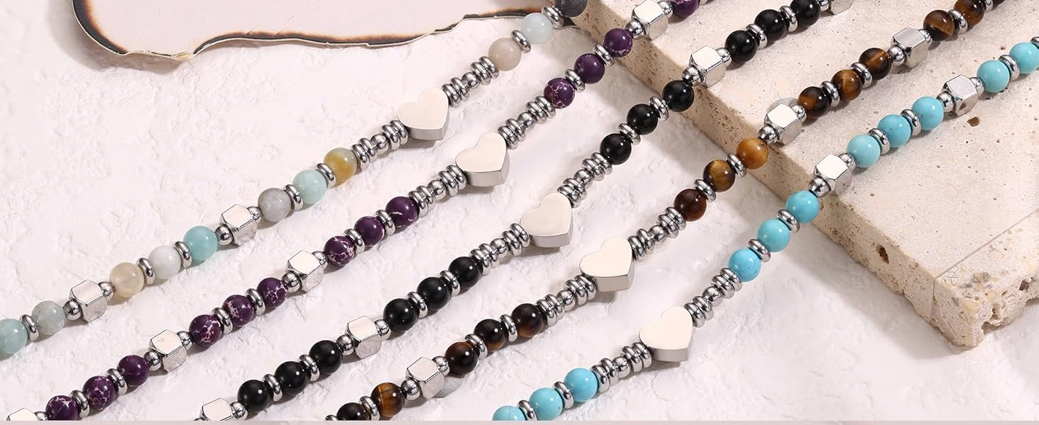 Plusieurs bracelets ou colliers de perles affichés en lignes parallèles. Les perles sont de différentes couleurs, notamment le violet, le noir, le marron et le bleu, entrecoupées de perles d'espacement argentées